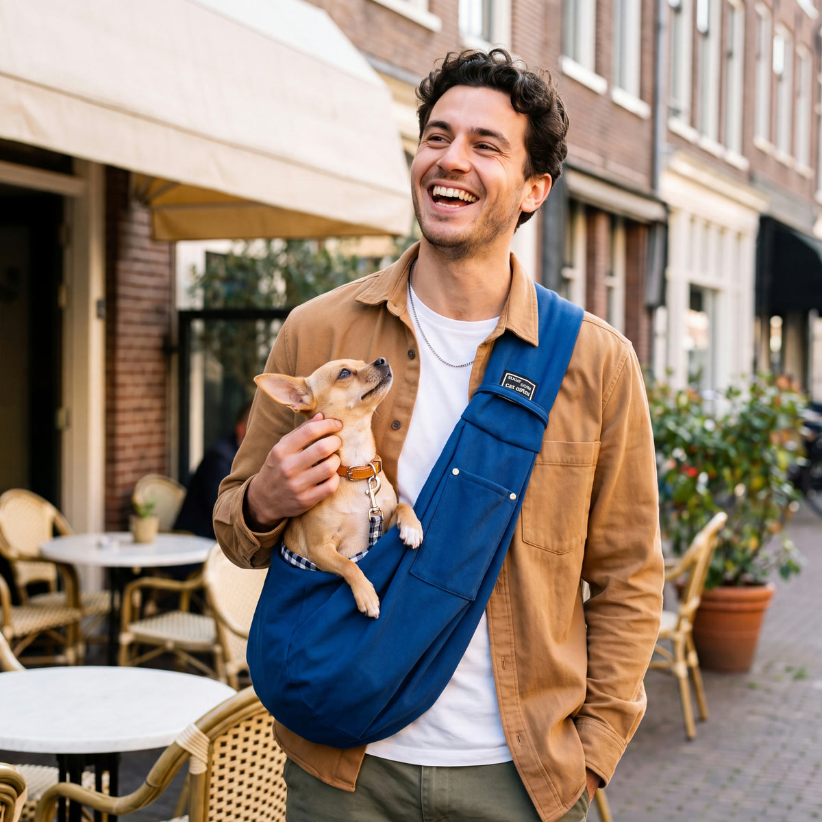 Jonge man op een terras met de blauwe schoudertas; de chihuahua in de tas kijkt naar hem op.