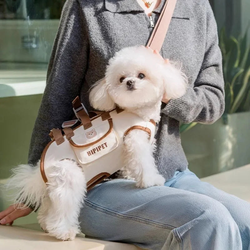 Bichon zit in de crèmekleurige draagtas over de schouder van een zittende vrouw.