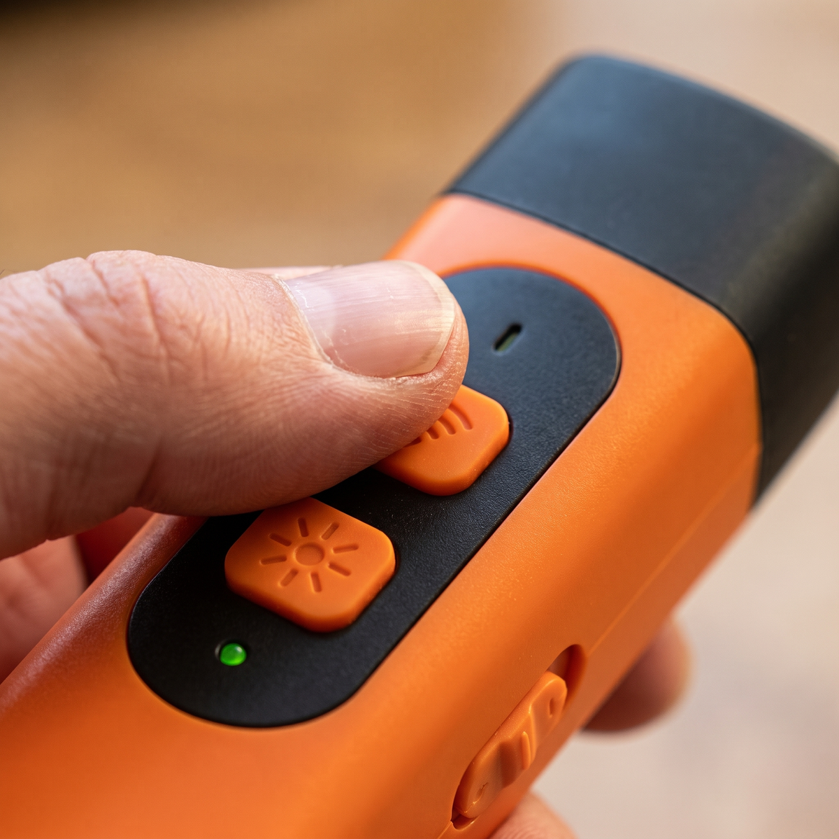 Van dichtbij: een duim op de bovenste oranje knop, met de tweede knop en het groene lampje eronder