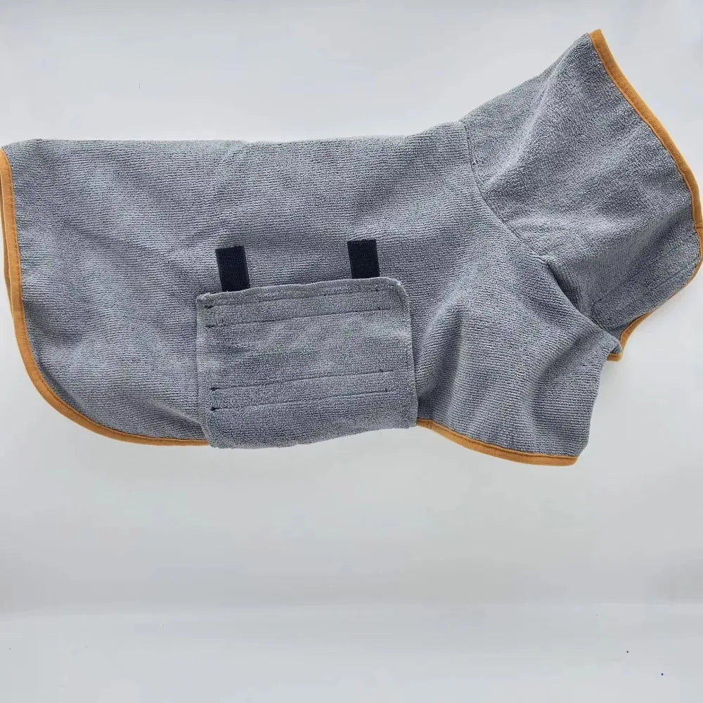 De grijze badjas met okergele bies plat neergelegd op een lichte ondergrond, met de buikband en de twee klittenbandsluitingen zichtbaar