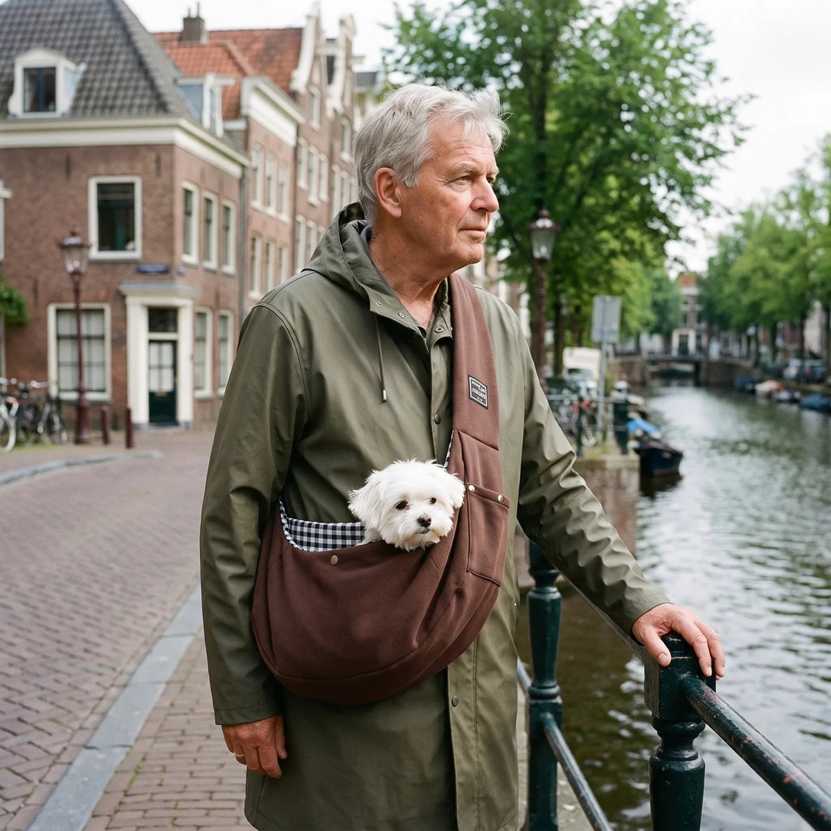 Man op de brug bij de gracht met de bruine schoudertas en een kleine witte hond.
