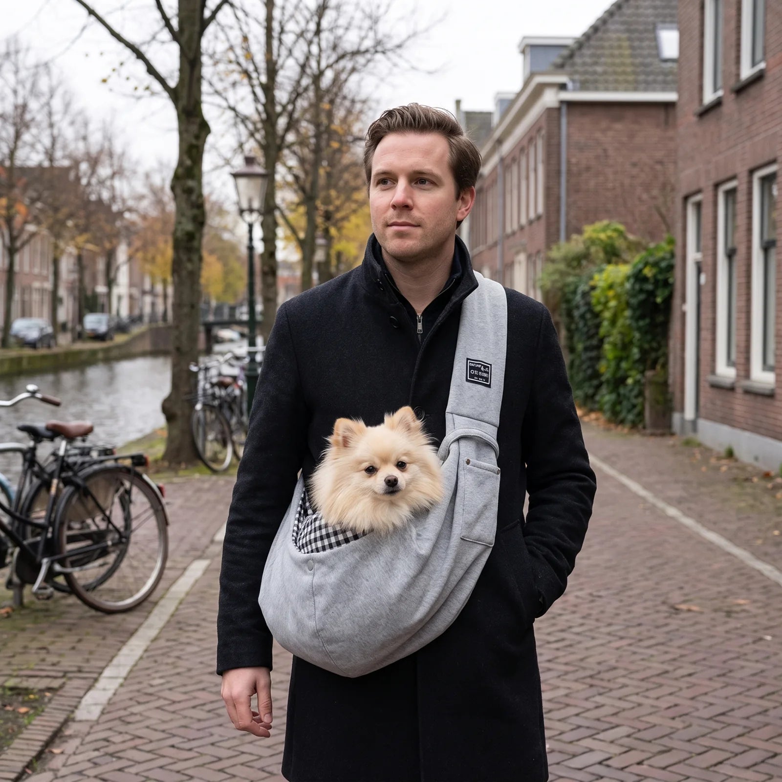 Jonge man draagt een kleine hond in de grijze schoudertas langs een gracht.